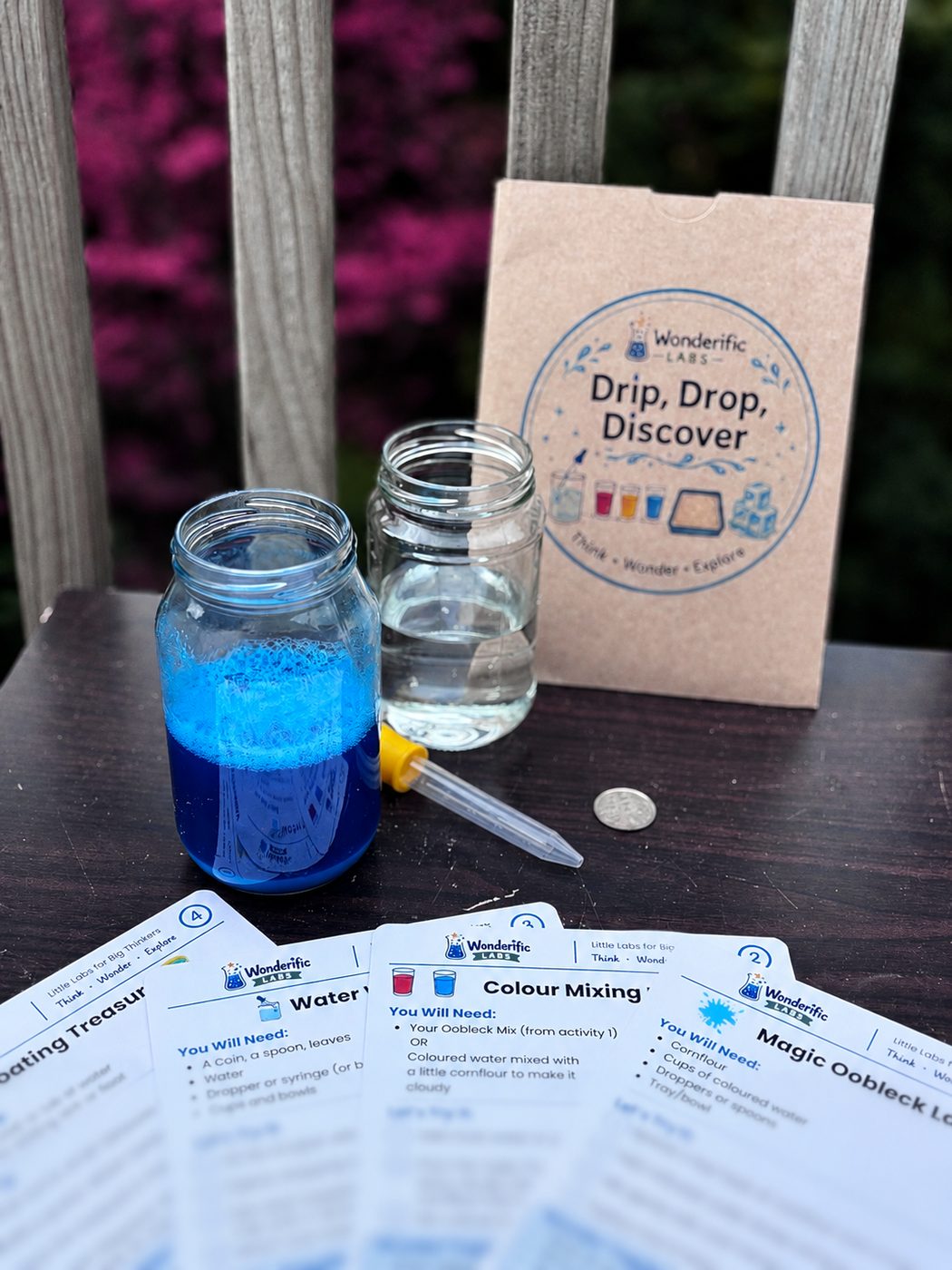 The Drip, Drop, Discover pack with jars of blue and clear water, a pipette and the activity cards laid out on a table