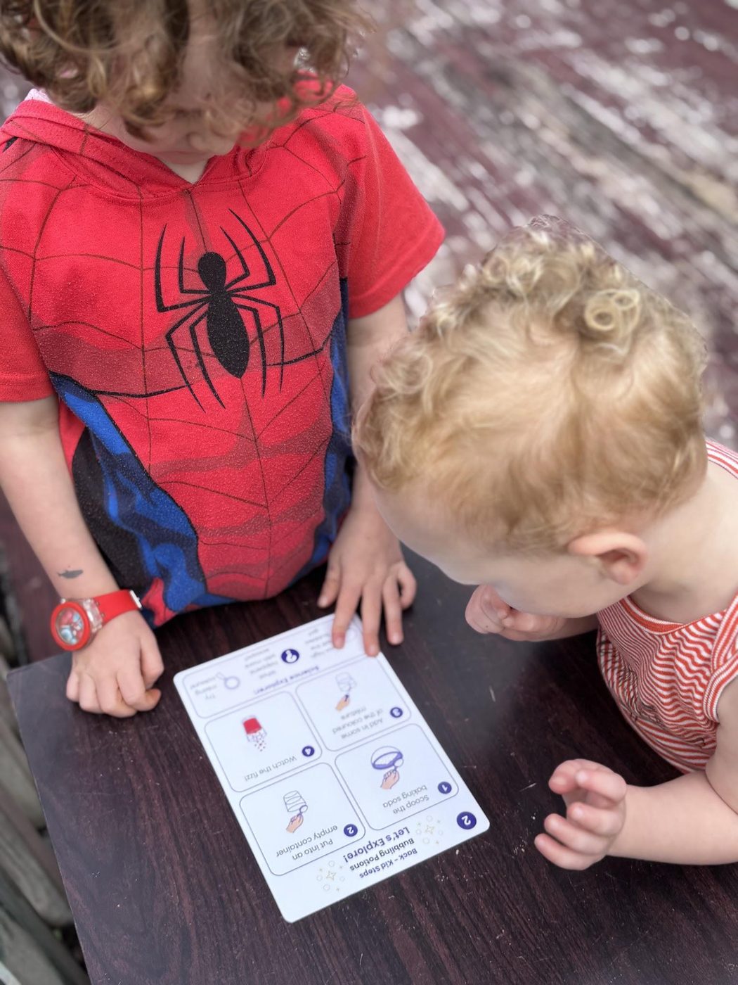 Two children with their heads together, reading a Magic and Mixtures activity card